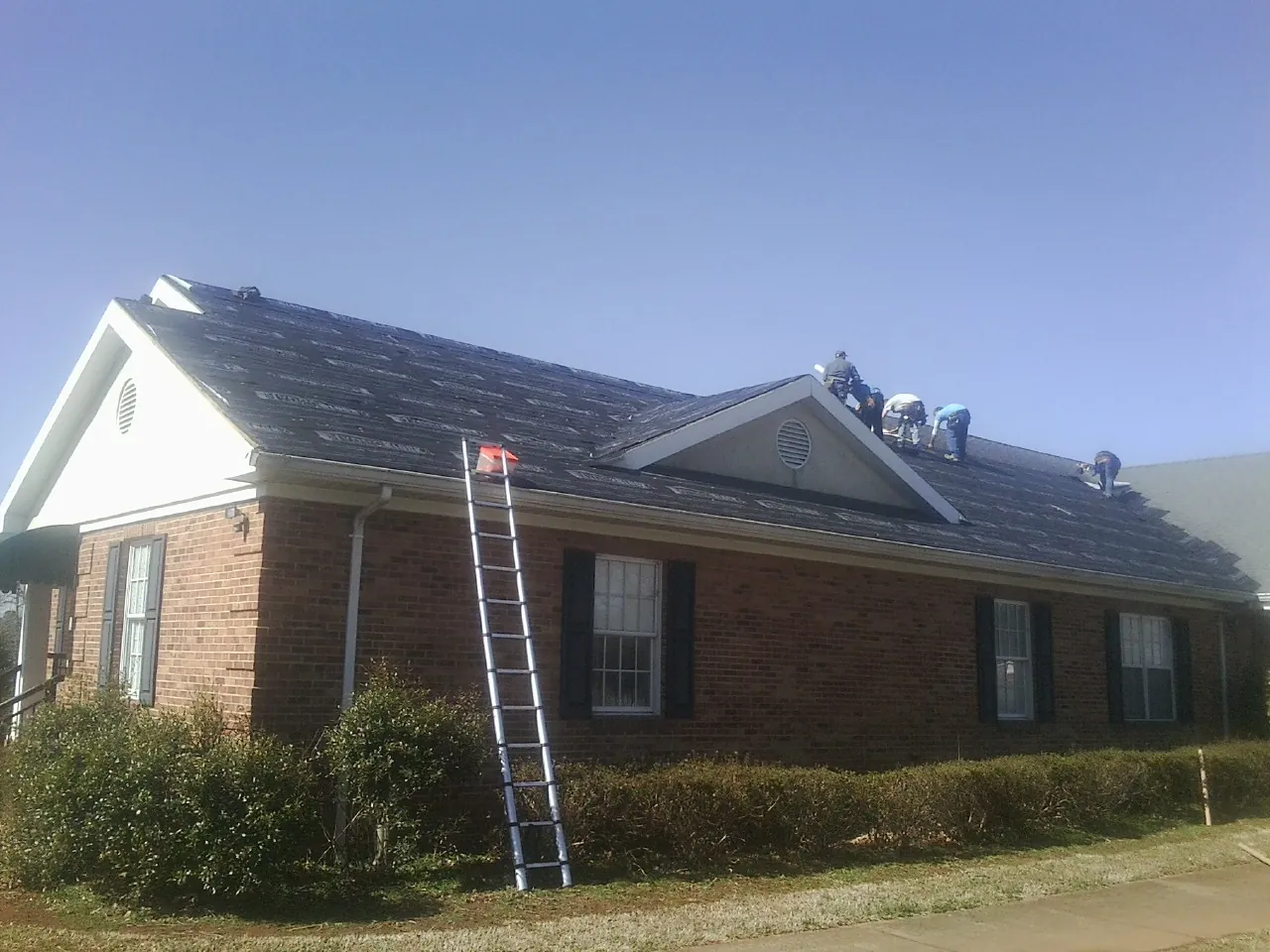 Crew tearing shingles off a brick ranch roof with a ladder set — Metal Roof Repair work by our crew in Wellington