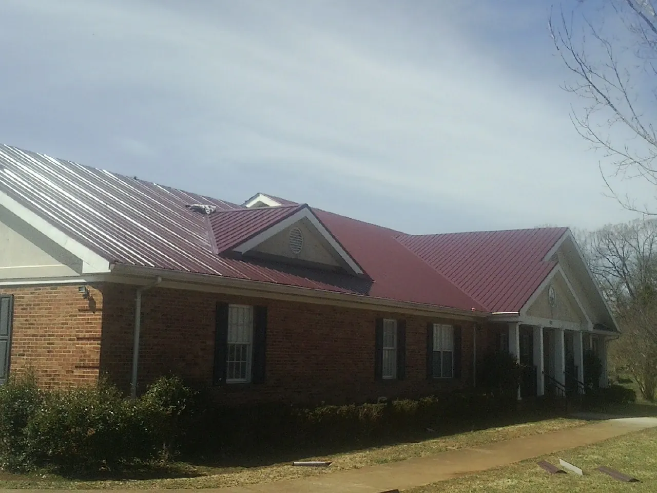 Red metal roof with gabled entries on a long brick building, from a Hail Damage Roof Repair job in Wellington