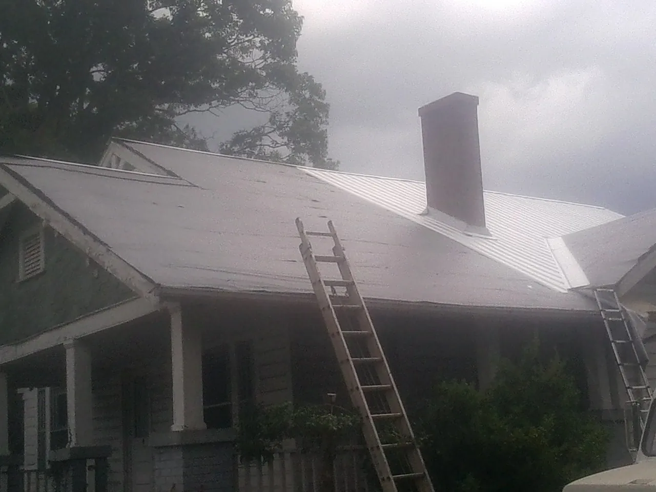 Ladders against a metal roof on an older home with a brick chimney in Wellington